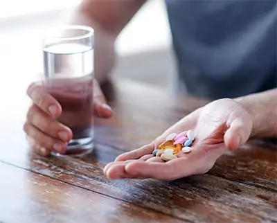  hombre con un puñado de suplementos y vaso de agua