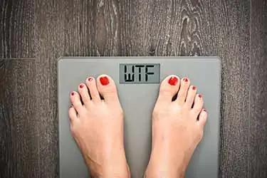 woman standing on body scale that reads WTF